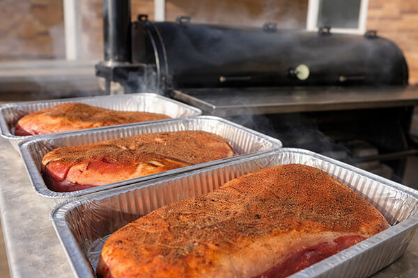bbq seasoning on meat next to a smoker